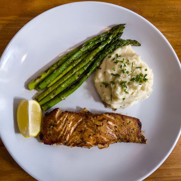 Grilled salmon with mashed potatoes, asparagus, and a lemon wedge on a white plate.