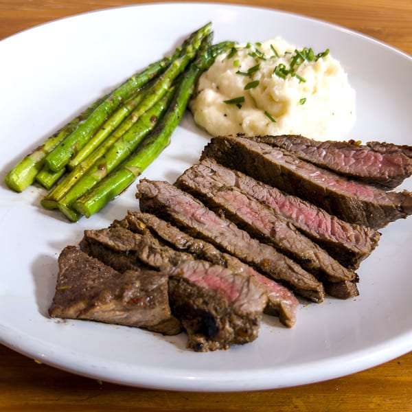 Sliced steak with asparagus and mashed potatoes on a white plate at Cafe La Tazita.