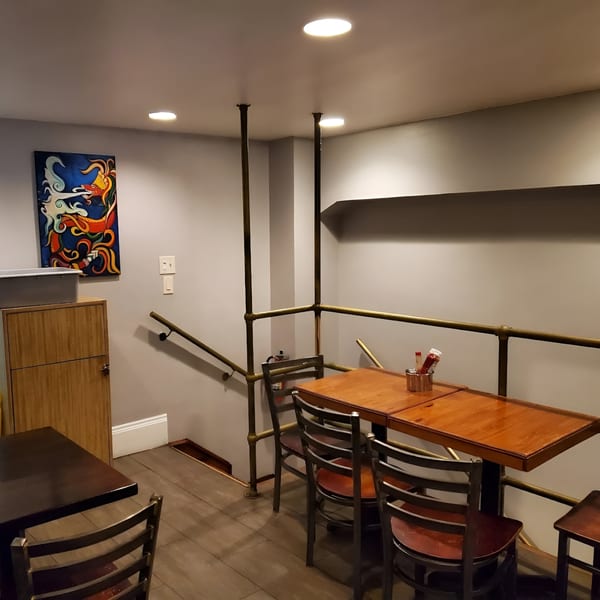 Cafe La Tazita's interior features wooden tables, metal chairs, a colorful painting, and a staircase with a railing.