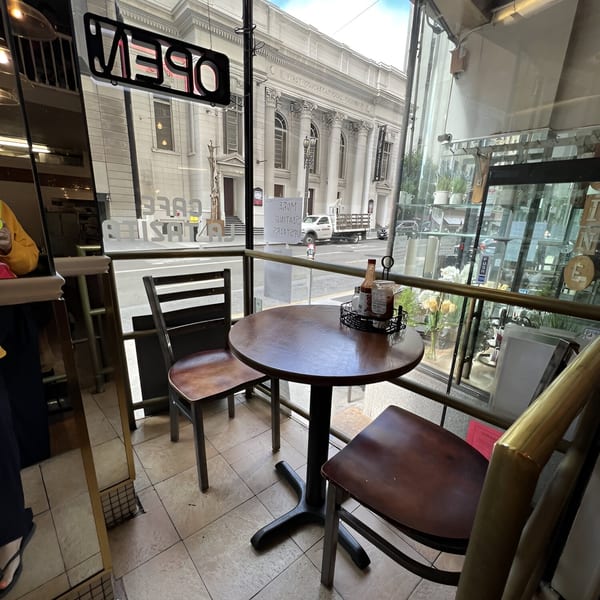 Cafe La Tazita's cozy corner table with street view of a grand building and an "OPEN" sign.