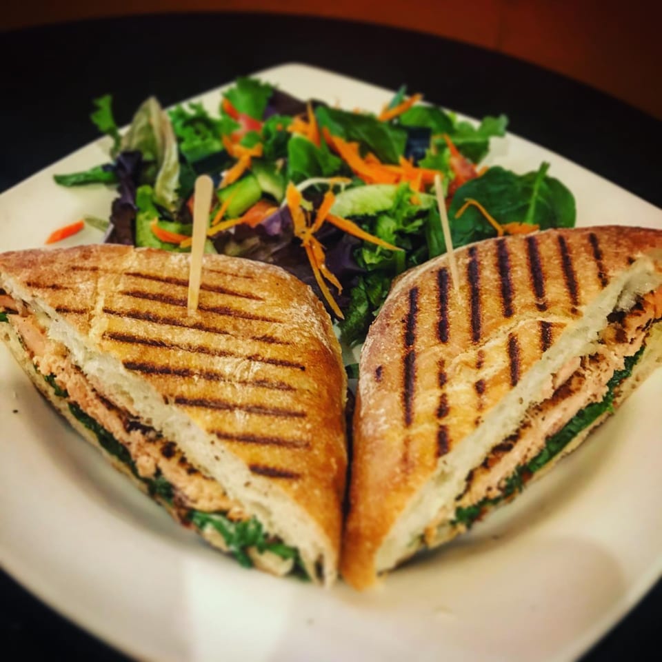 Grilled panini sandwich cut in half with a side salad on a white plate at Cafe La Tazita.