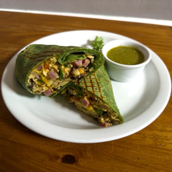 A Cafe La Tazita breakfast burrito, cut in half, revealing eggs, ham, and cheese, with green sauce.