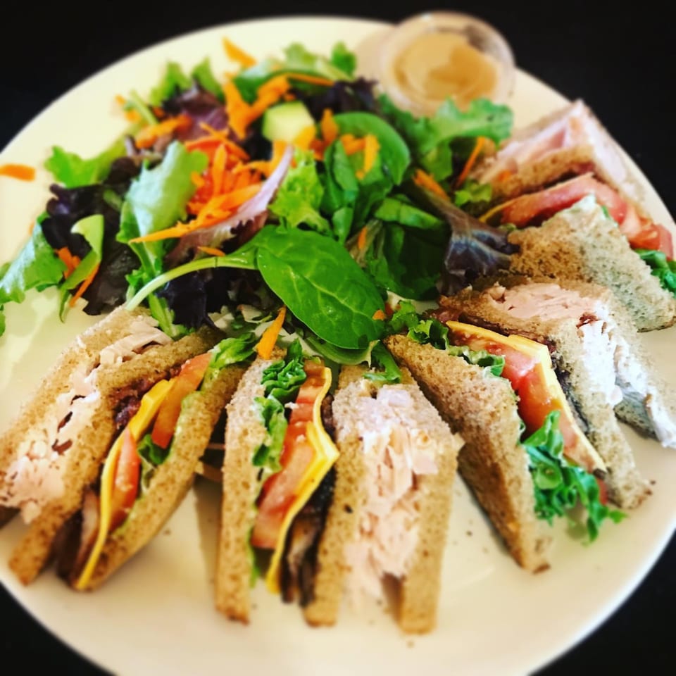 A plate of Cafe La Tazita's club sandwiches with salad and dressing.